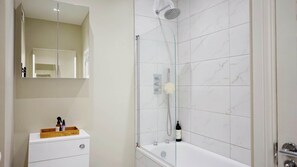 Une salle de bain avec une douche en marbre blanc, un lavabo blanc avec un porte-savon en bois et un miroir au-dessus du lavabo.