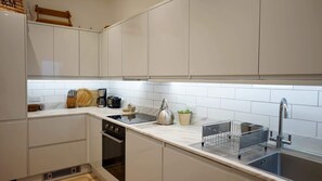 A modern kitchen with white cabinets, a stainless steel kettle, a coffee maker, and a sink. - Spacious 1BDR Garden Flat in Charlton (London)