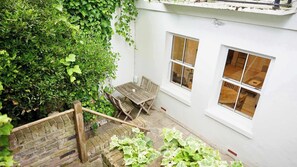 Un bâtiment blanc avec une table et des chaises en bois, un escalier en briques et une fenêtre.