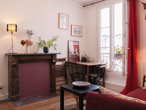 Ein Zimmer mit Kamin, Esstisch, Stühlen, einer Couch, einem Fenster mit Blick auf Gebäude und einem roten Vorhang.