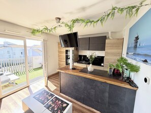 Une cuisine moderne dotĂ©e dâun tĂ©lĂ©viseur Ă Ă©cran plat, dâun comptoir en bois et offrant une vue sur la mer grĂące Ă une grande fenĂȘtre.