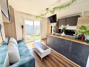 Een moderne woonkamer met een bank, een salontafel, een televisie en een keukenhoek met een aanrecht en planten.