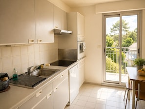 A kitchen with a sink, stove, oven, and a view of greenery through a sliding glass door. - Sea & Pines Apt with Terrace (La Baule-Escoublac)