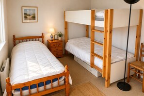 A bedroom with a bunk bed, a single bed, a bedside table with a lamp, a framed picture on the wall, and a chair. - Sea & Pines Apt with Terrace (La Baule-Escoublac)