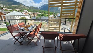 A balcony with a table set for breakfast, chairs, and a view of a town with mountains in the background. - Bright, new apartment with a terrace 3* (Briançon)
