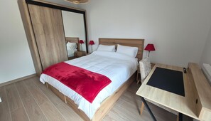 Ein Schlafzimmer mit einem Bett, einem Spiegel, zwei Nachttischen mit Lampen und einem Schreibtisch mit Stuhl.