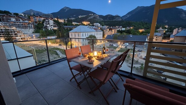 A balcony with a table set for dining, overlooking a town and mountains. - Bright, new apartment with a terrace 3* (Briançon)