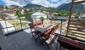 A balcony with a table and chairs, overlooking a town with buildings and mountains. - Bright, new apartment with a terrace 3* (Briançon)