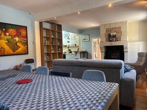 A living room with a sofa, a dining table with a patterned tablecloth, a bookshelf, and a fireplace. - House with garden near Honfleur (Gonneville-sur-Honfleur)