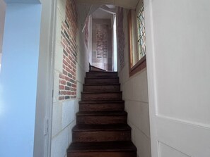 Eine Treppe mit Holzstufen führt zu einem Raum mit Backsteinwand und einem Fenster mit Metallgitter.