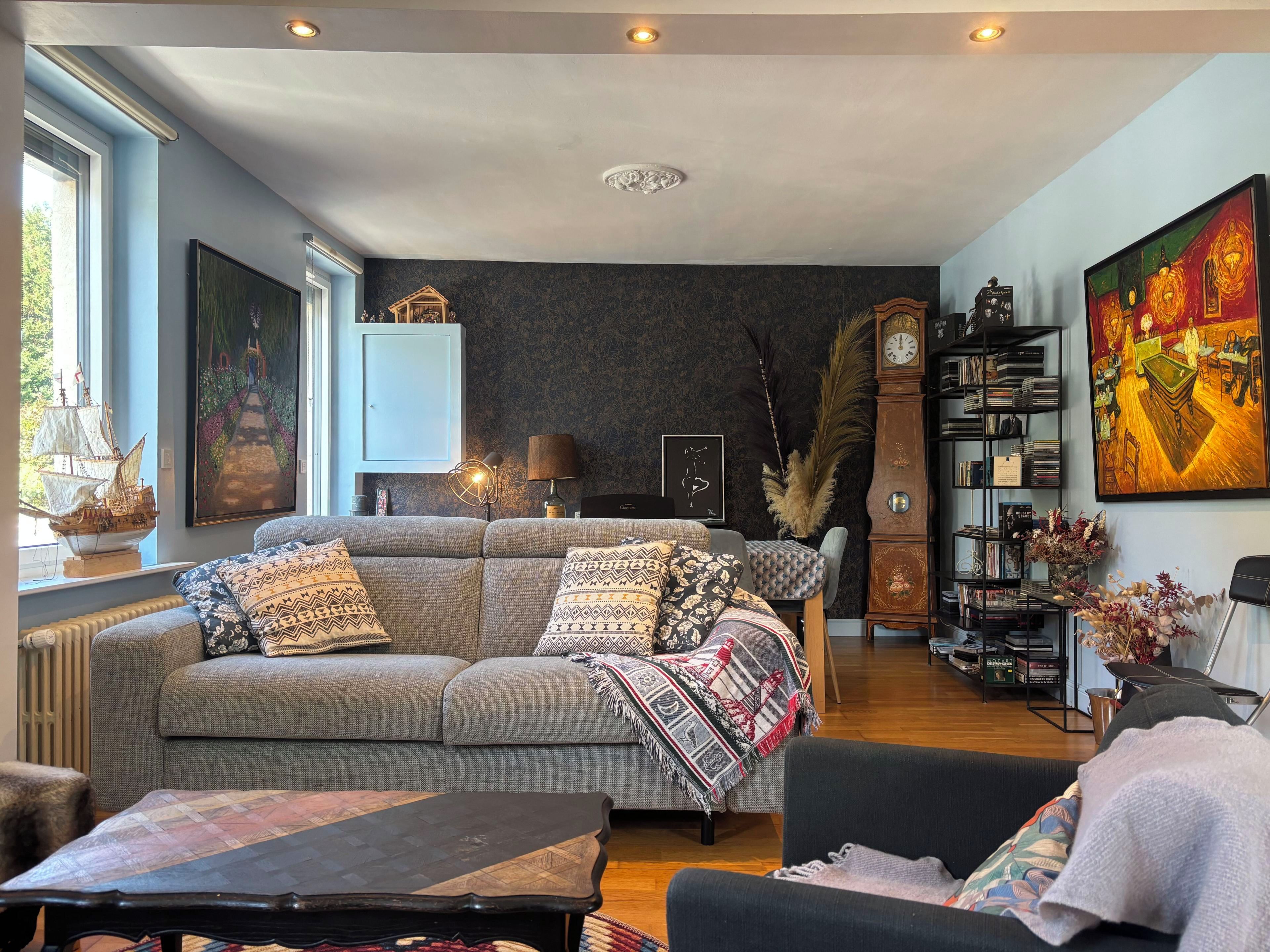 Un salon comprenant un canapé, une table basse, une bibliothèque et un grand tableau accroché au mur.