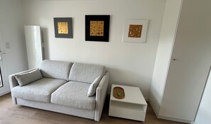 Una sala de estar con un sofá gris, una mesita auxiliar blanca con una bandeja de madera y tres obras de arte enmarcadas en la pared.