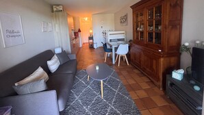 A living room with a sofa, a coffee table, a cabinet, and a kitchen in the background. - Garden studio with terrace, 600m from the port (Saint-Raphaël)