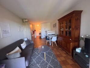 A living room with a sofa, a coffee table, a cabinet, and a kitchen in the background. - Garden studio with terrace, 600m from the port (Saint-Raphaël)