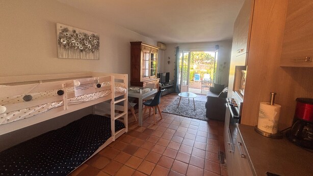 A room with bunk beds, a dining table, chairs, a TV, and a view of the outdoors. - Garden studio with terrace, 600m from the port (Saint-Raphaël)
