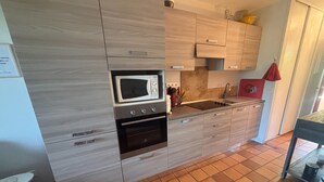 A kitchen with a microwave, oven, sink, and wooden cabinets. - Garden studio with terrace, 600m from the port (Saint-Raphaël)