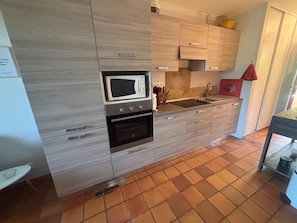 A kitchen with a microwave, oven, sink, and wooden cabinets. - Garden studio with terrace, 600m from the port (Saint-Raphaël)