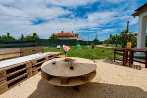 Un tavolo rotondo in legno con un vaso di fiori e biscotti, circondato da bancali di legno e un'area ghiaiosa.