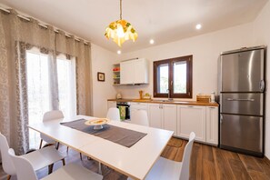 Una cucina moderna con mobili bianchi, un frigorifero in acciaio inossidabile e una zona pranzo con tavolo e sedie bianche.