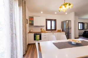 Una cucina moderna con mobili bianchi, forno integrato, frigorifero e zona pranzo con tavolo e sedie.