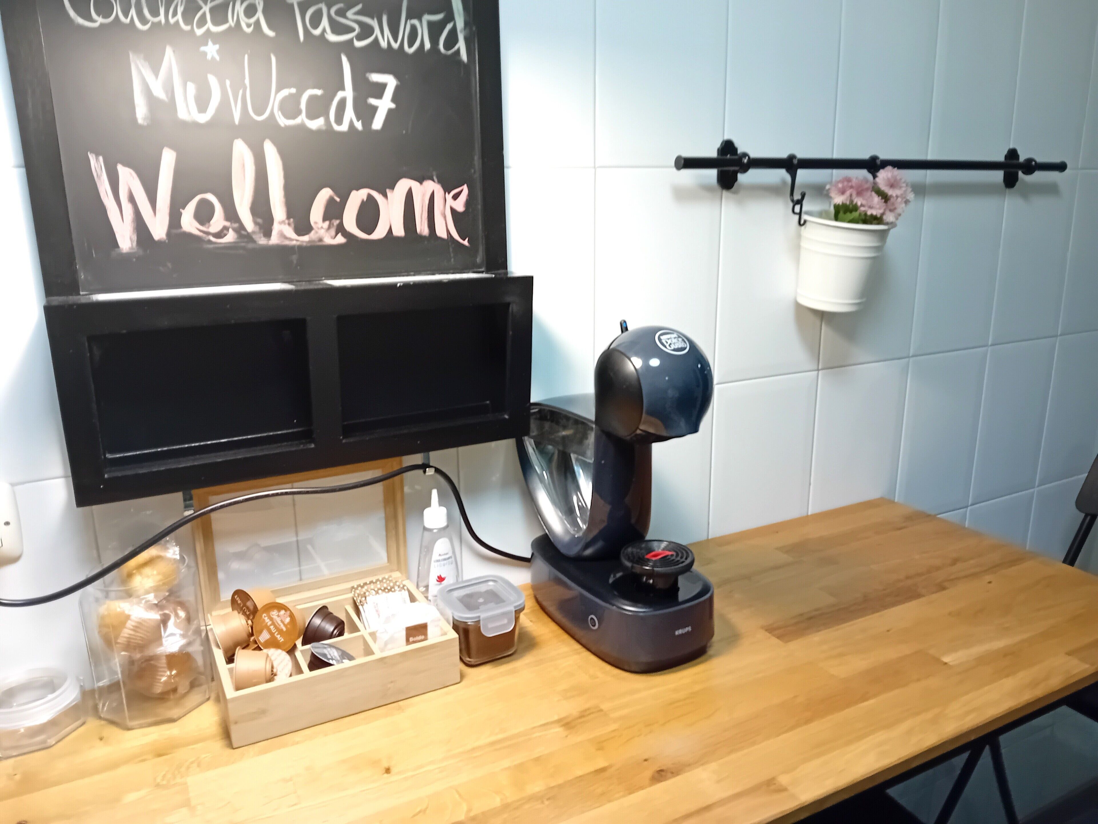 A kitchen counter with a coffee machine, a chalkboard with a password, and a basket of pastries.