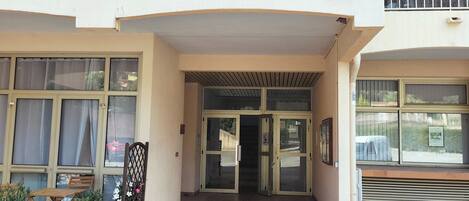A building entrance with a covered porch, a staircase leading inside, and a sign with the letter 'Da'.