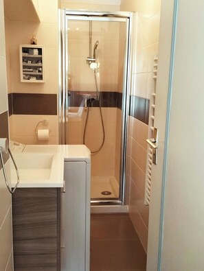 Een badkamer met een douche met glazen wand, een witte wastafel en een handdoekhouder.