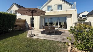 Ein zweistöckiges Haus mit einer Terrasse, Gartenmöbeln und einem großen Sonnenschirm.