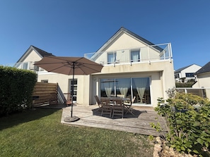 Ein zweistöckiges Haus mit einer Terrasse, Gartenmöbeln und einem großen Sonnenschirm.