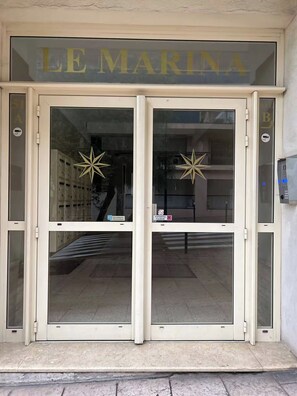 Ein Gebäudeeingang mit dem Schild 'LE MARINA' über zwei Glastüren, jede mit einer Sterndekoration.
