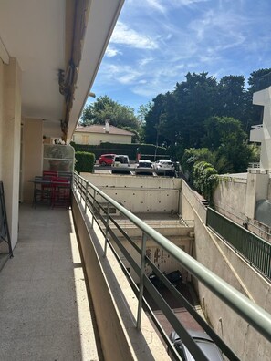 Ein Balkon mit Blick auf parkende Autos und ein Gebäude mit einem Ziegeldach.
