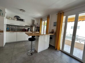 Eine moderne Küche mit Kochinsel, weißen Schränken und Blick auf einen Balkon.