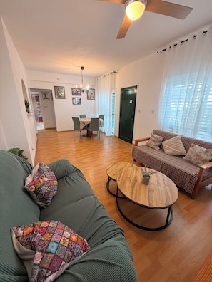 Ein Wohnzimmer mit einer Couch, einem runden Couchtisch, einem karierten Sofa und einem Essbereich mit Tisch und Stühlen.