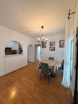Ein geräumiger Essbereich mit einer Chandelier, einem runden Tisch und Stühlen. Durch einen Bogen ist eine Küche sichtbar.