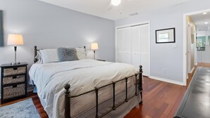 A bedroom with a bed, bedside lamps, a ceiling fan, a wardrobe, and a framed picture on the wall. - Blue Bayou B (Fort Myers Beach)