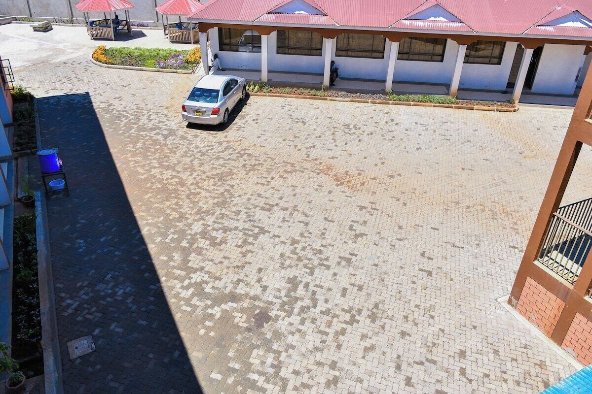 Um edifício com um pátio pavimentado, um carro branco estacionado em frente e uma área coberta com telhados vermelhos.