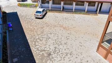 Um edifício com um pátio pavimentado, um carro branco estacionado em frente e uma área coberta com telhados vermelhos.