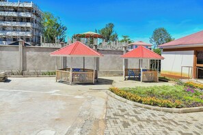 A courtyard with two wooden gazebos, a paved area, and a flower bed.