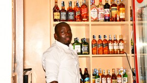 A man standing in front of a shelf with various liquor bottles. - Hotel Tausi (Rodi Kopany)