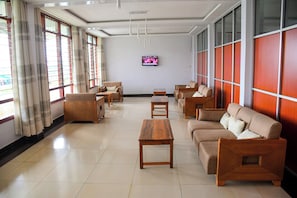 A spacious room with a sofa set, wooden tables, and a TV on the wall.