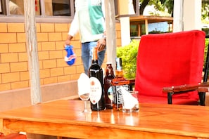 A wooden table with bottles and glasses, a red chair, and a person in the background. - Hotel Tausi (Rodi Kopany)