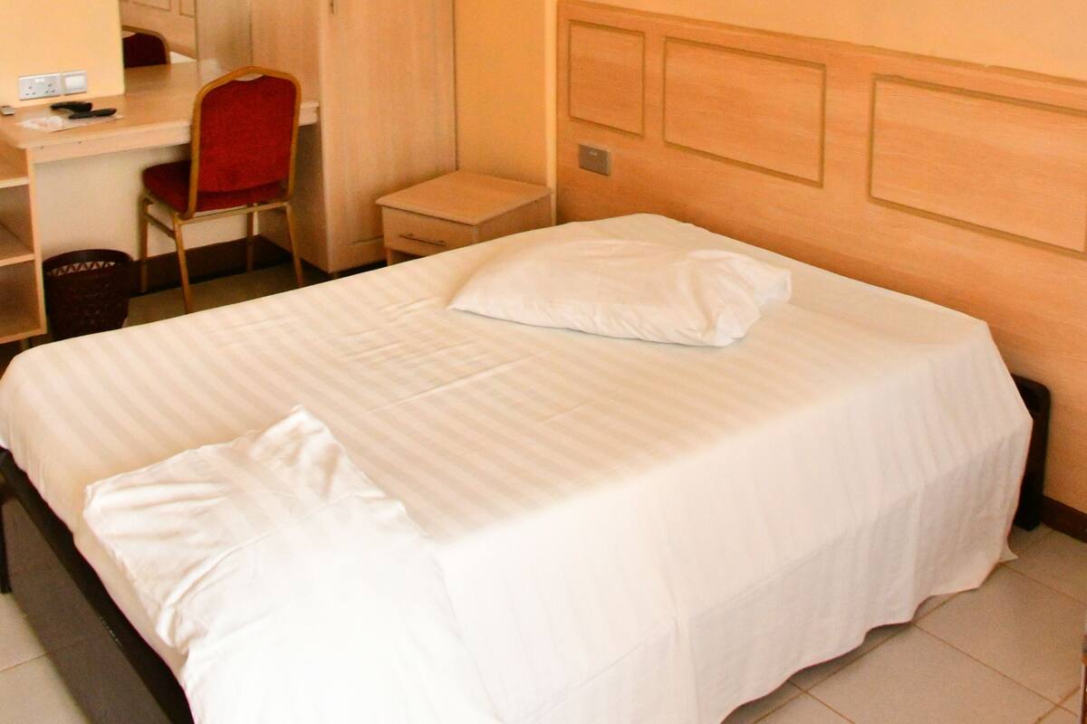 Una habitación de hotel con cama, escritorio, silla, armario y mosquitero.