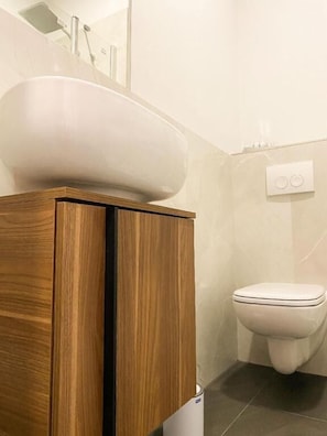Ein Badezimmer mit einem Holzkosmetikschrank, einem weißen Waschbecken und einer Toilette.