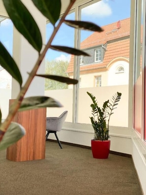 Ein Zimmer mit großem Fenster, einem Blumentopf, einem Sessel und einem Holztisch.