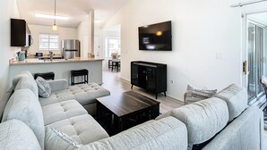 A modern living room with a sectional sofa, a coffee table, a flat-screen TV mounted on the wall, and a kitchen area in the background. - Luxury beach 2-bedroom condo in highly sought Cape Canaveral community  (Cape Canaveral)