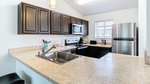 A kitchen with dark cabinets, stainless steel appliances, a granite countertop, and a hanging pendant light. - Luxury beach 2-bedroom condo in highly sought Cape Canaveral community  (Cape Canaveral)