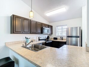 A kitchen with dark cabinets, stainless steel appliances, a granite countertop, and a hanging pendant light. - Luxury beach 2-bedroom condo in highly sought Cape Canaveral community  (Cape Canaveral)