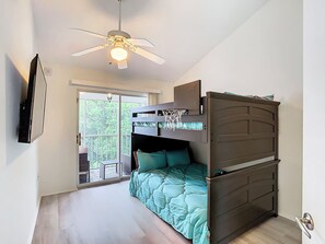 A bedroom with a bunk bed, a ceiling fan, a TV mounted on the wall, and a balcony with a view of greenery. - Luxury beach 2-bedroom condo in highly sought Cape Canaveral community  (Cape Canaveral)