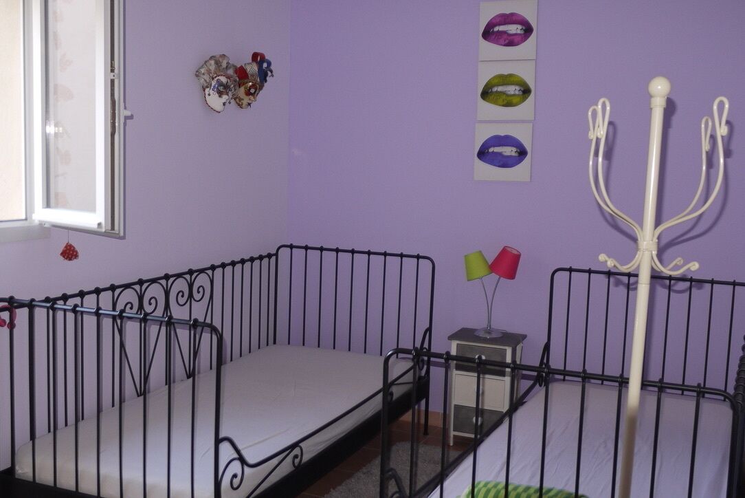 Une chambre d’enfant avec un berceau, une petite table avec une lampe et des décorations murales, notamment des motifs de lèvres et un porte-manteau.