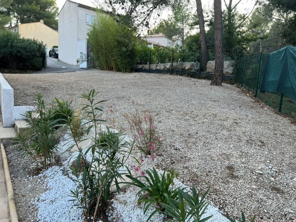 A gravel yard with a white building, some greenery, and a fence.